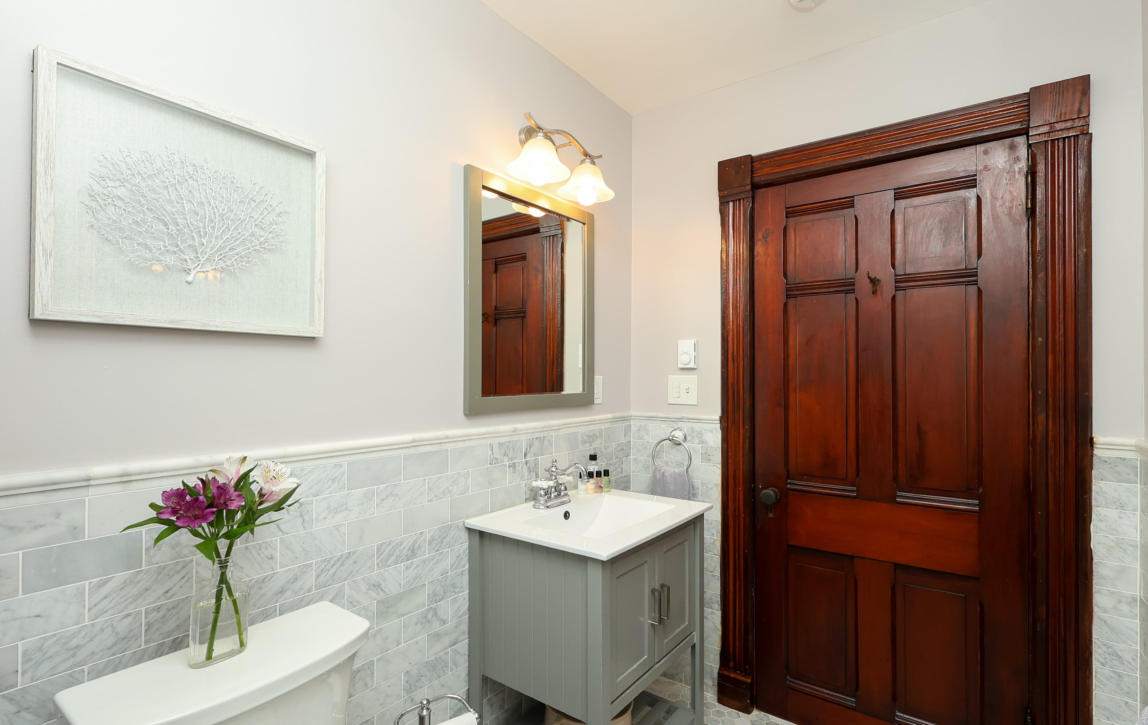 Modern bathroom with gray cabinetry, marble accents, and a decorative wall art above a sink.