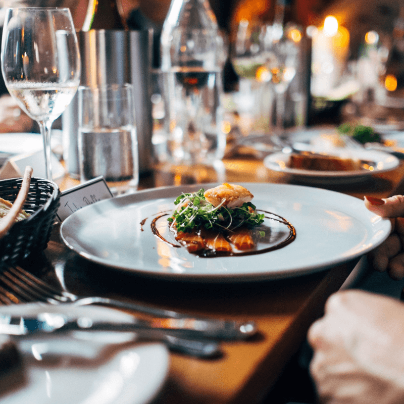 A beautifully plated dish with greens and sauce served at an elegantly set dining table.