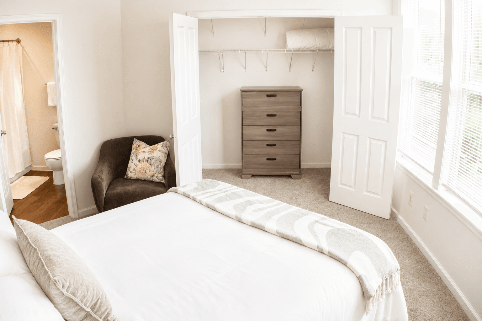 Bright and cozy bedroom featuring a bed, a chair, a dresser, and a closet.