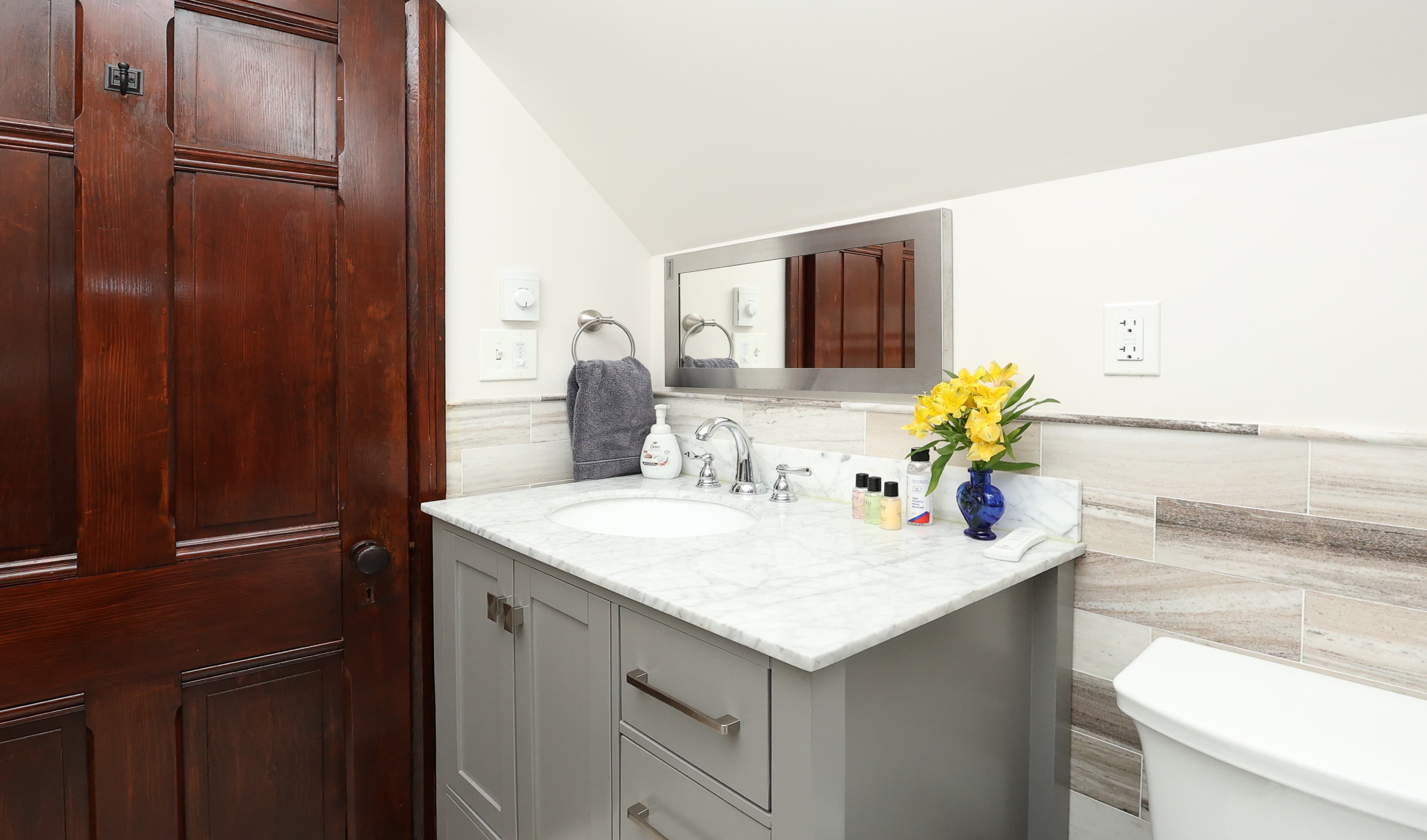 A modern bathroom featuring a marble countertop, a small vase of flowers, and a wooden door.