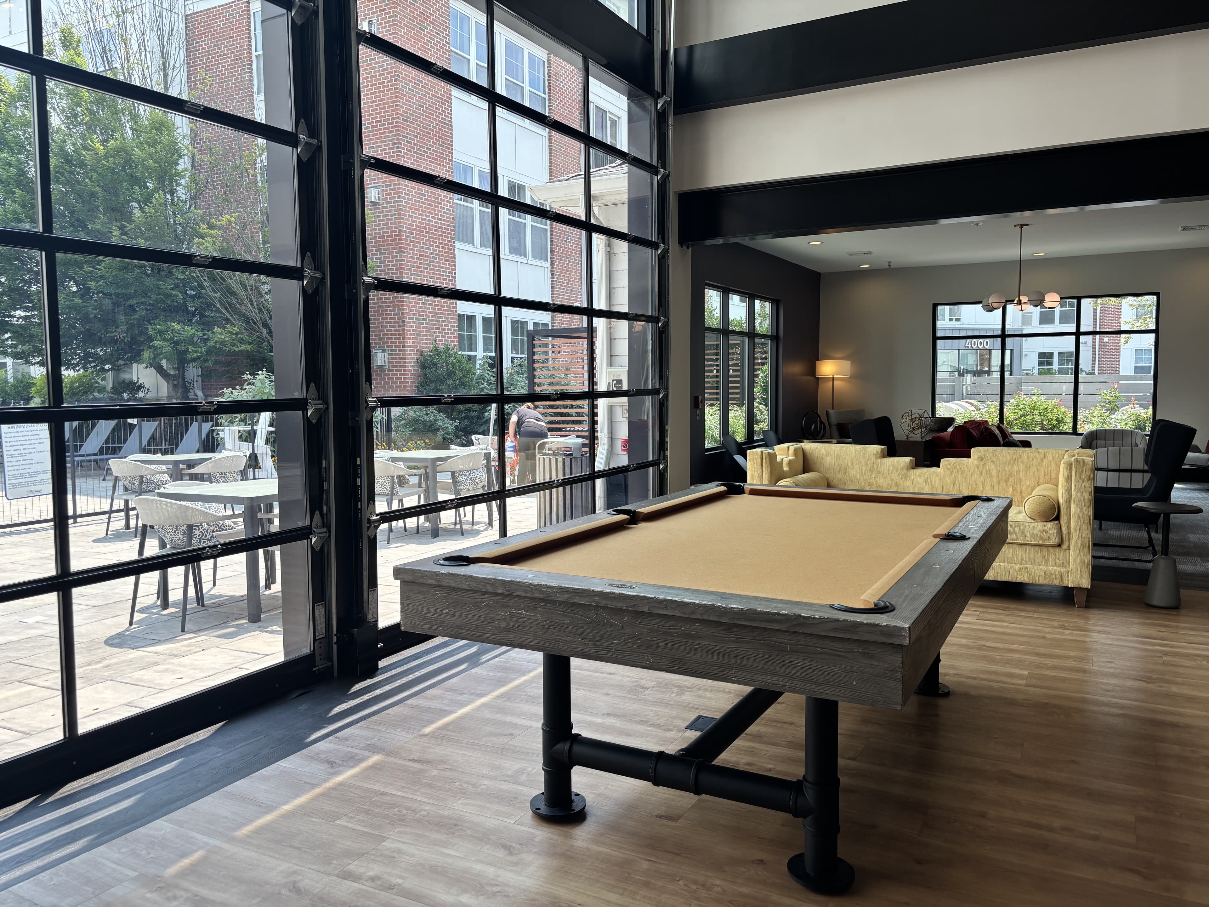 Interior view of a stylish lounge with a pool table and large windows overlooking an outdoor patio.