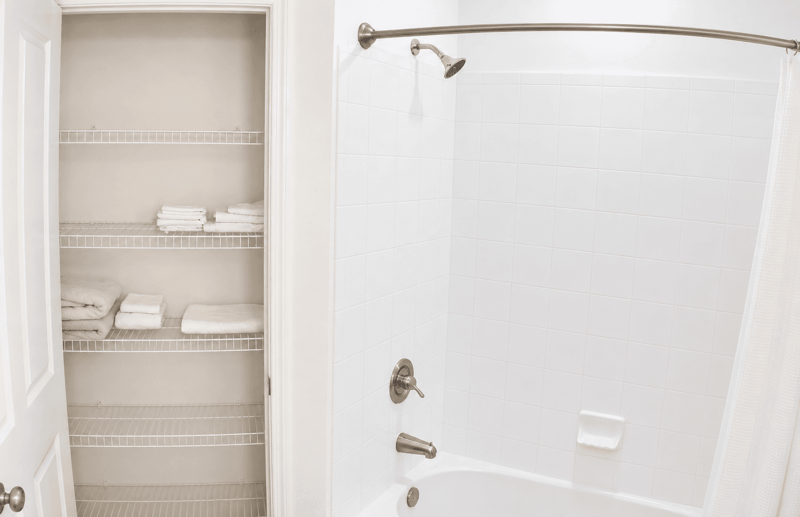 A clean bathroom featuring a shower and a shelf with neatly folded towels.