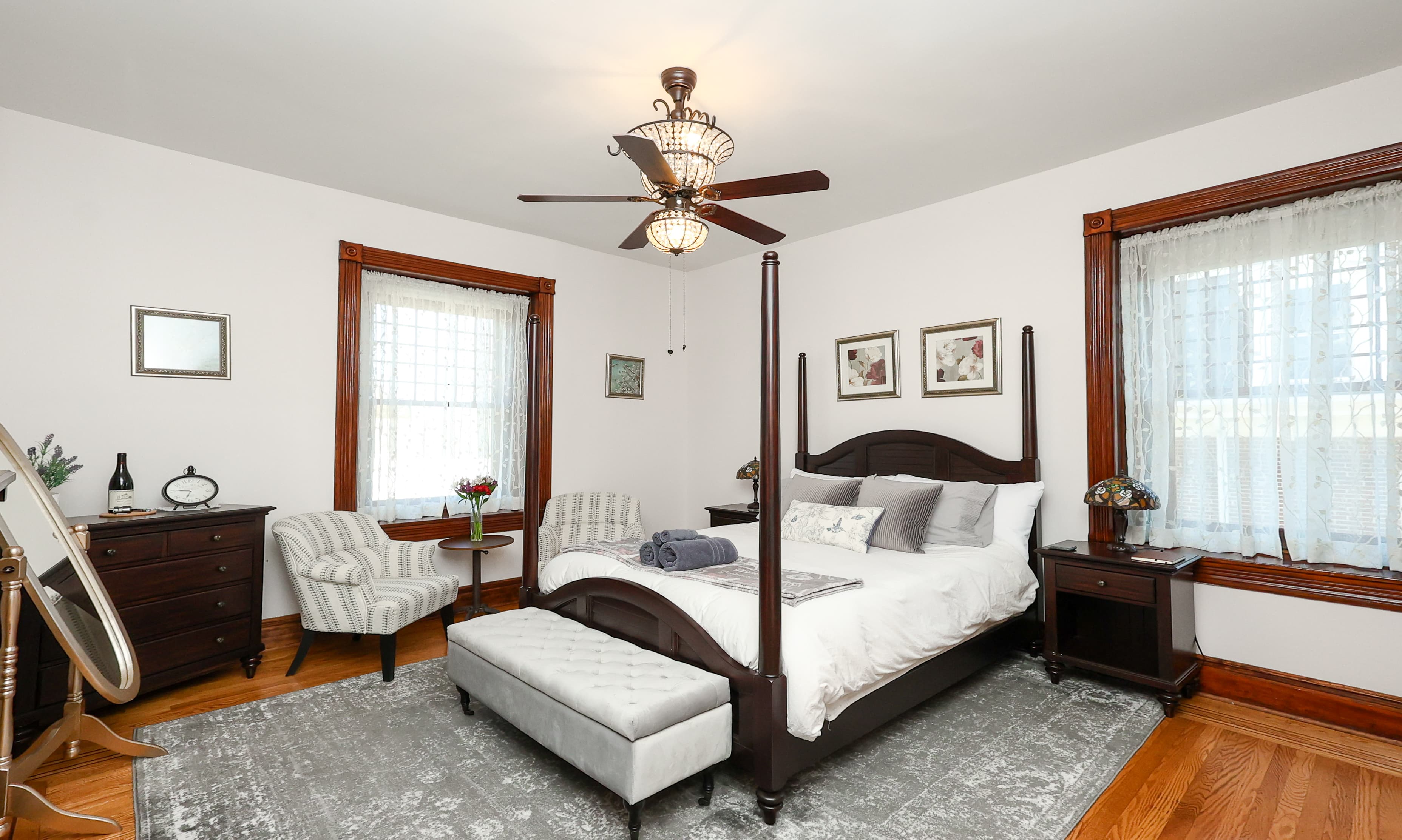 A cozy bedroom featuring a four-poster bed, elegant furnishings, and natural light from two windows.
