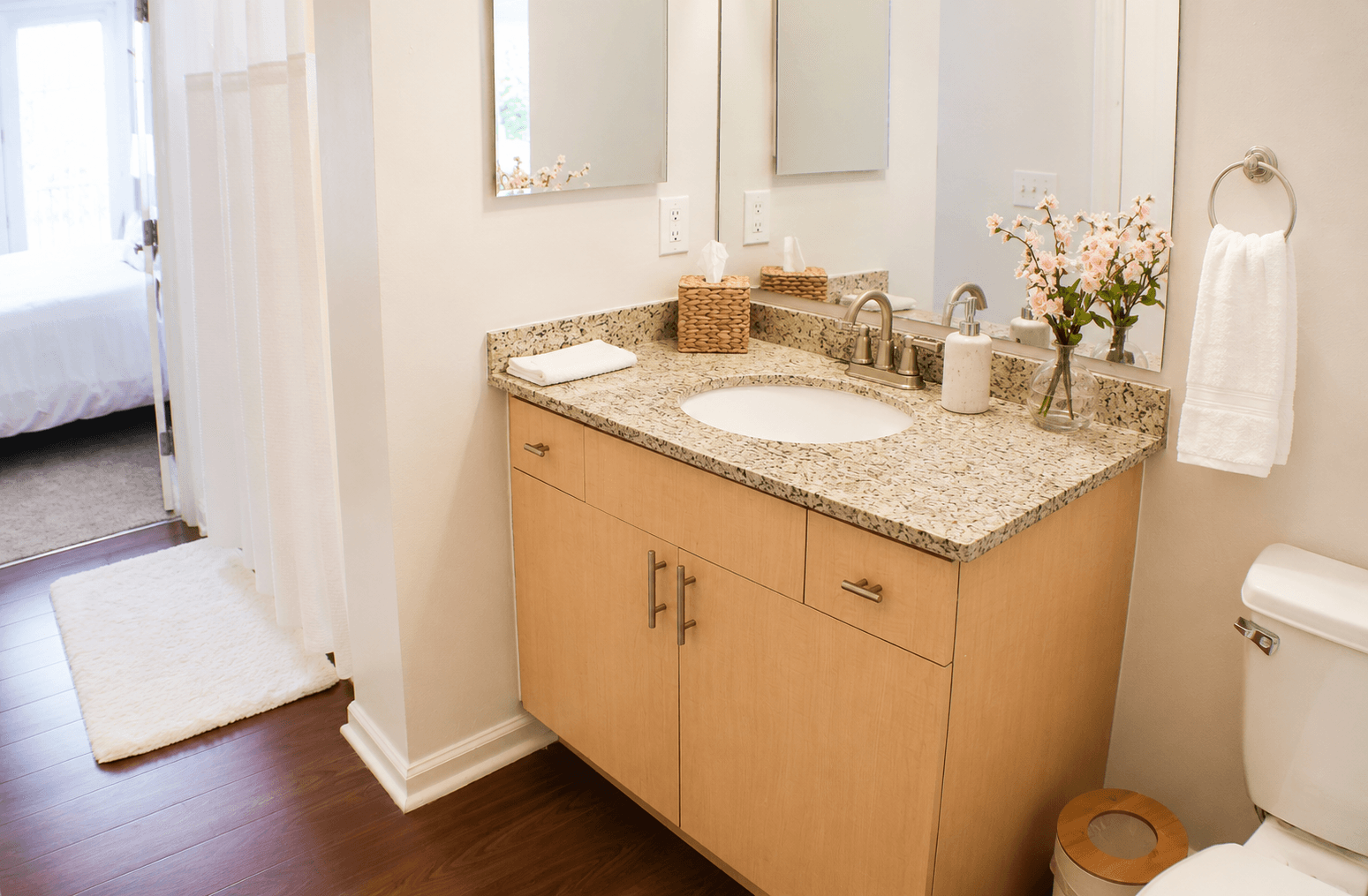 A bright, modern bathroom features a granite sink countertop, wooden cabinetry, and floral decor.