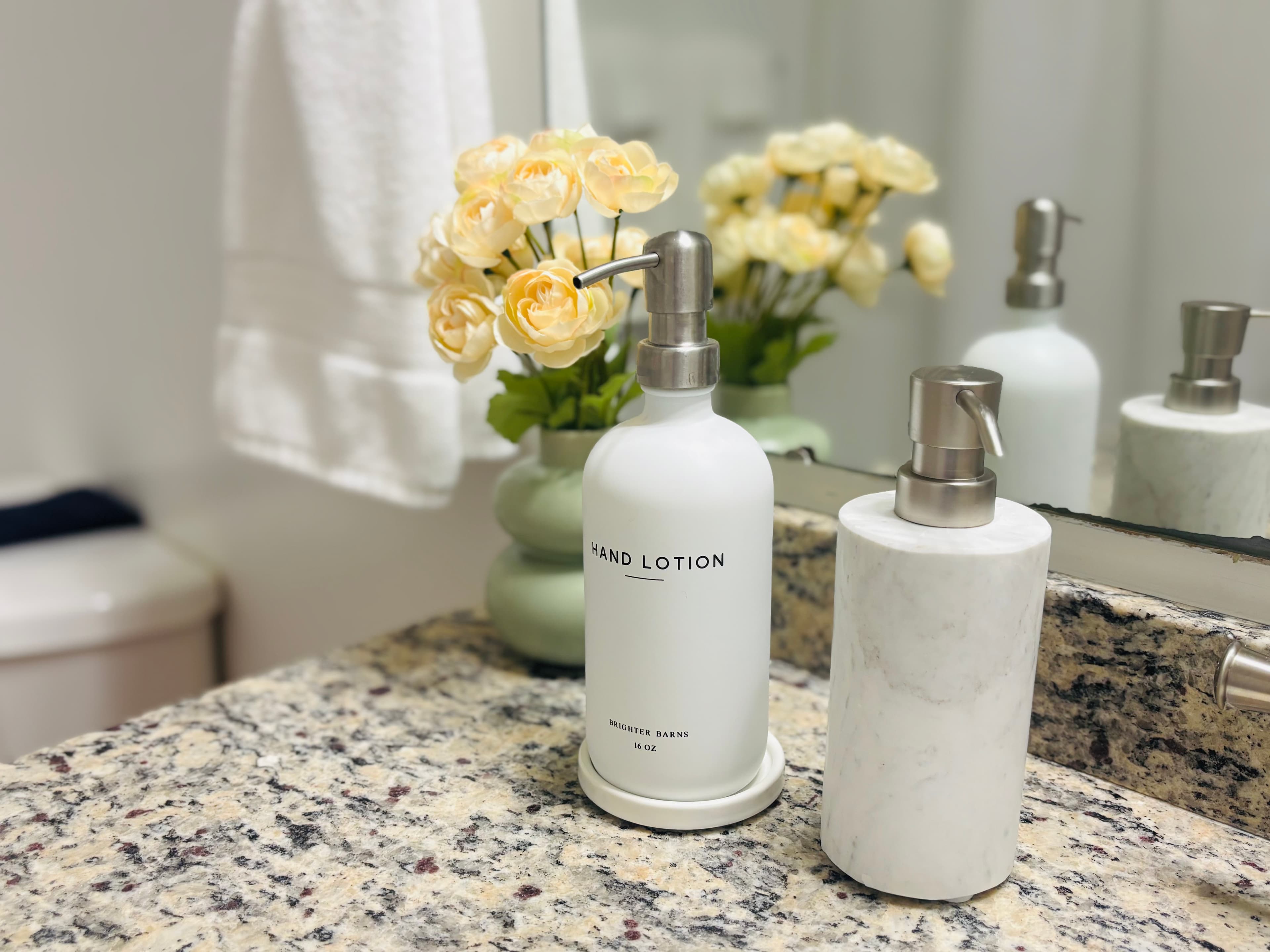 A bathroom countertop featuring hand lotion and a decorative floral arrangement.