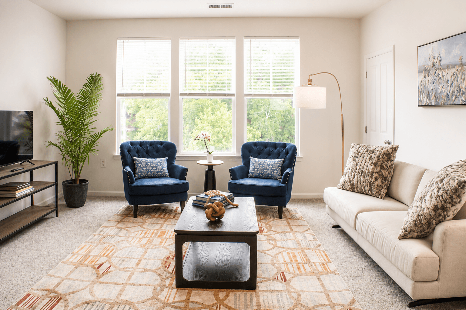Bright living room featuring two blue chairs, a white sofa, a coffee table, and large windows.