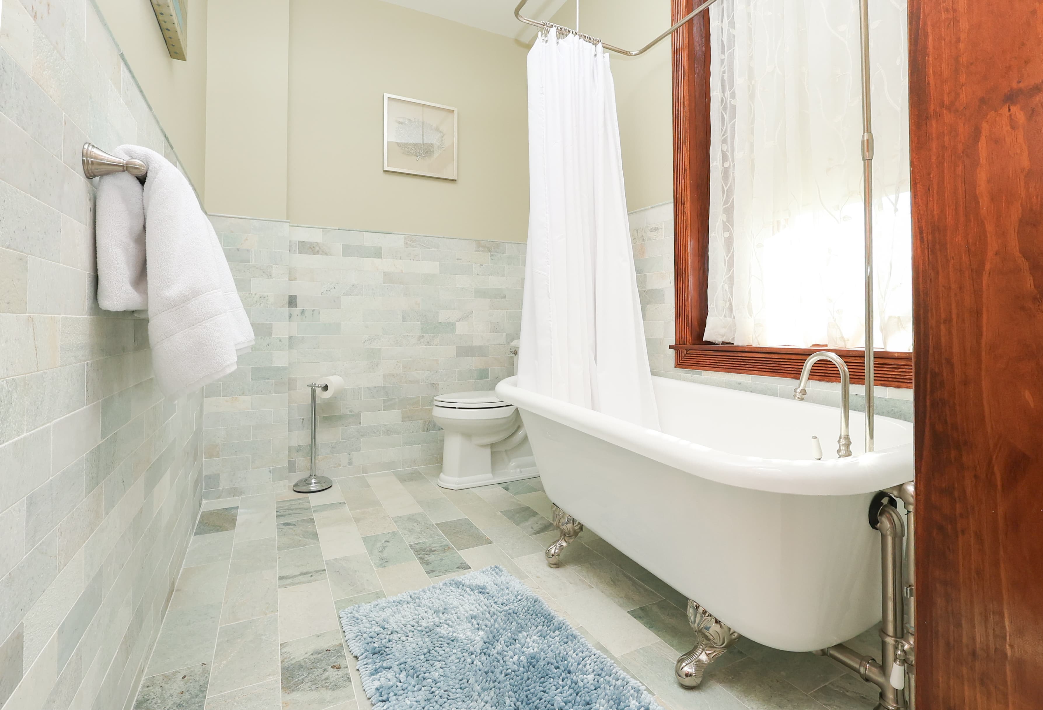 A modern bathroom featuring a freestanding tub, shower with white curtain, and tiled walls.
