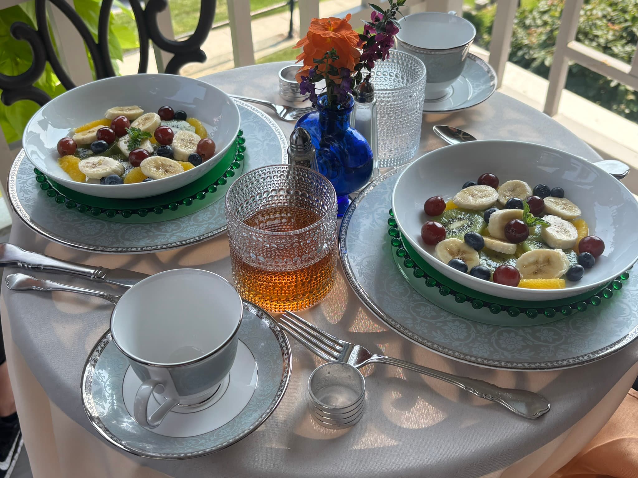 A beautifully set table with two bowls of fruit, a tea cup, and decorative flowers.