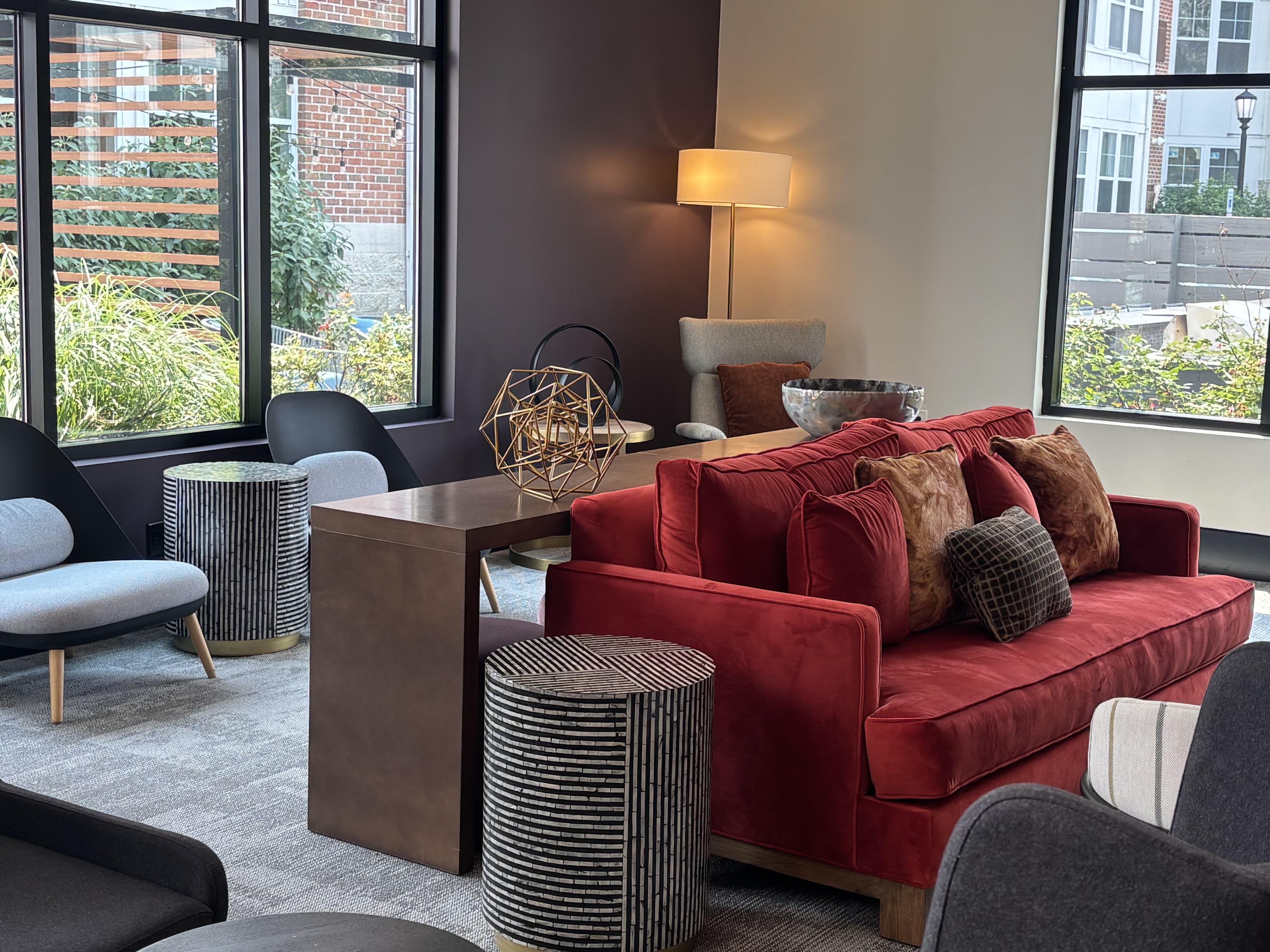 A cozy lounge area featuring a red sofa, modern chairs, a small table, and decorative elements near large windows.