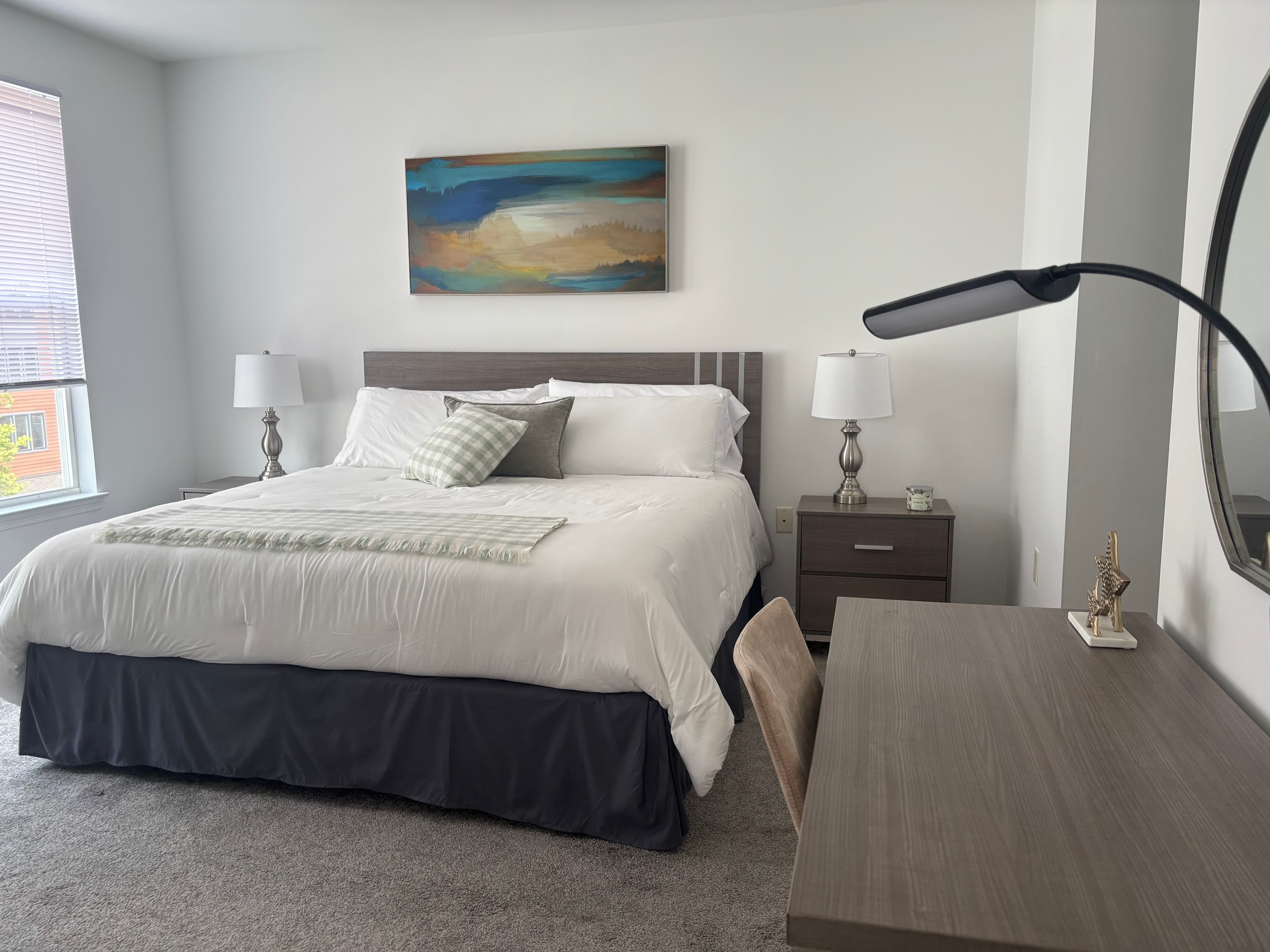 A modern bedroom featuring a large bed, two lamps, a desk, and abstract wall art.