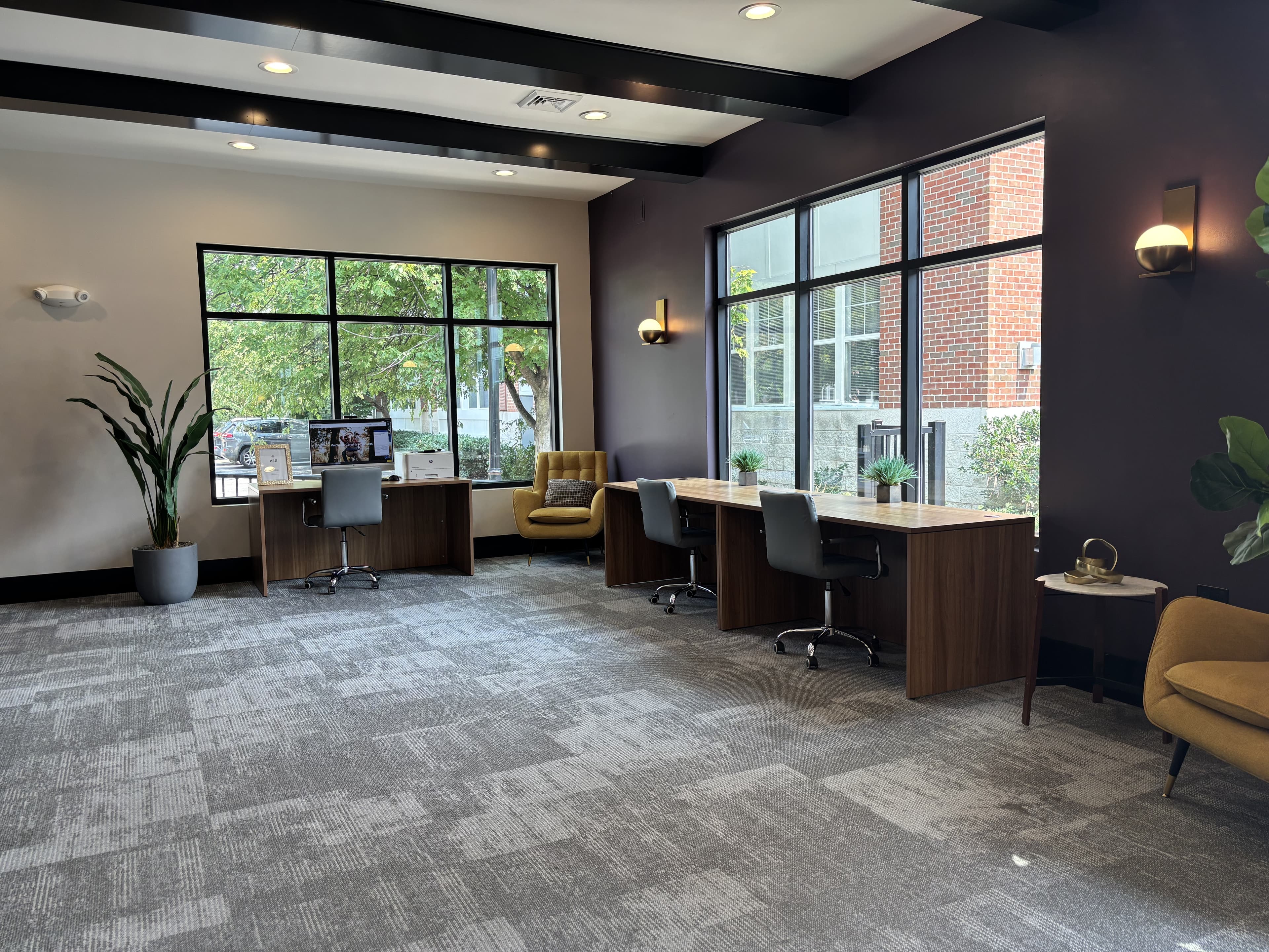 Modern office space featuring two workstations, comfortable seating, and large windows with outdoor views.