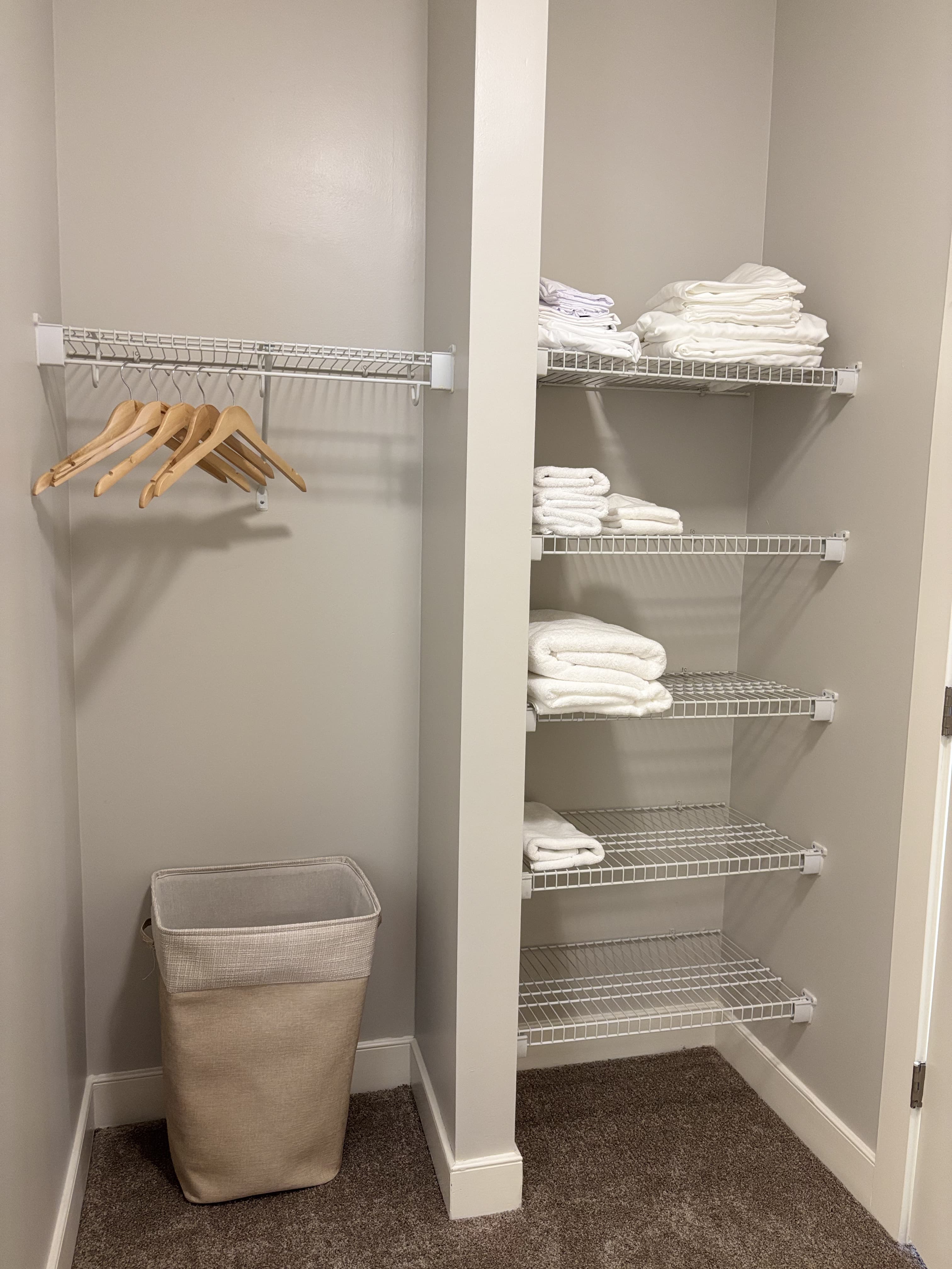A neatly organized closet with a hanging rack, shelves of folded towels, and a laundry basket.