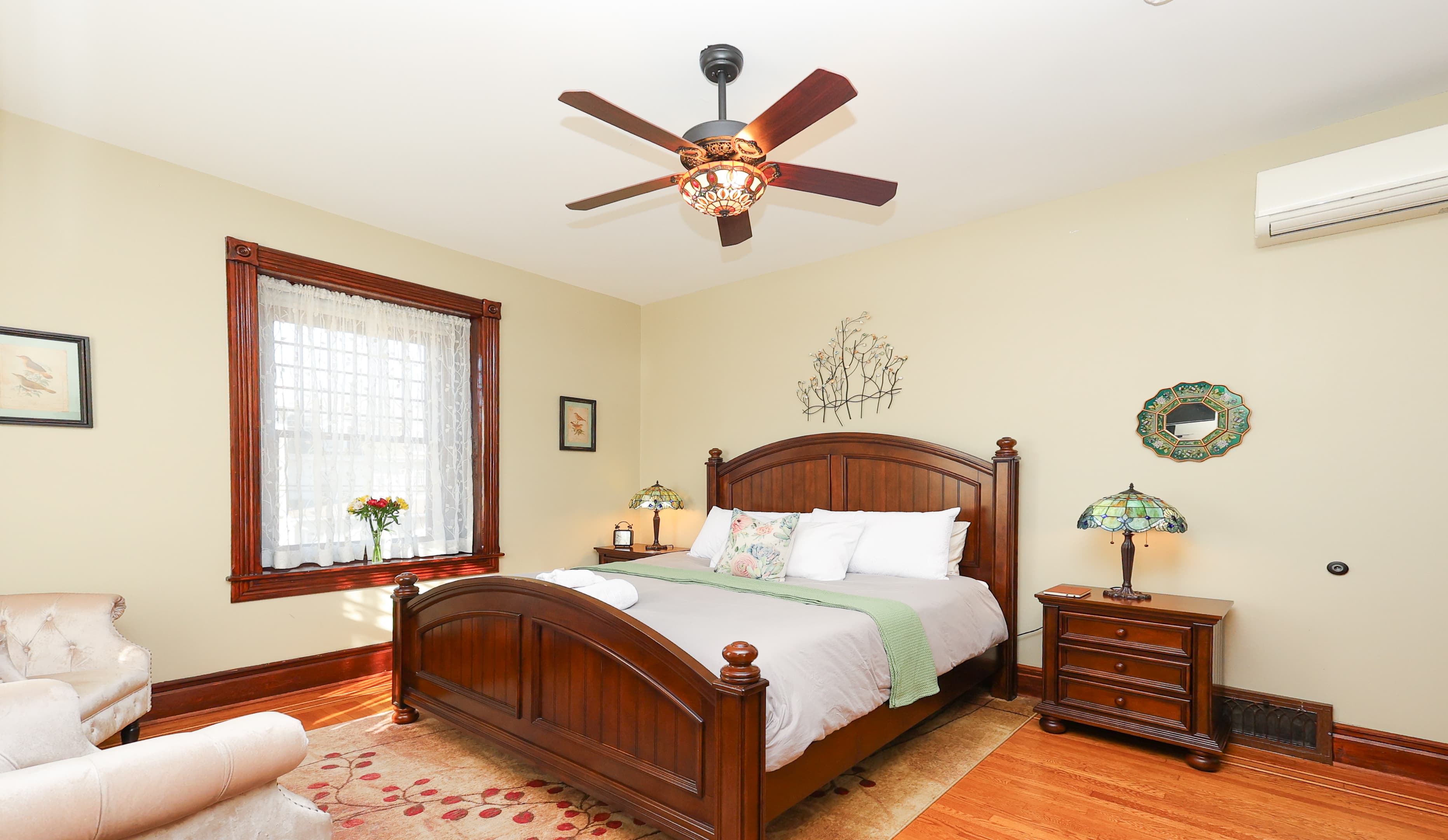 A cozy bedroom featuring a wooden bed, decorative lamps, and natural light from a window.