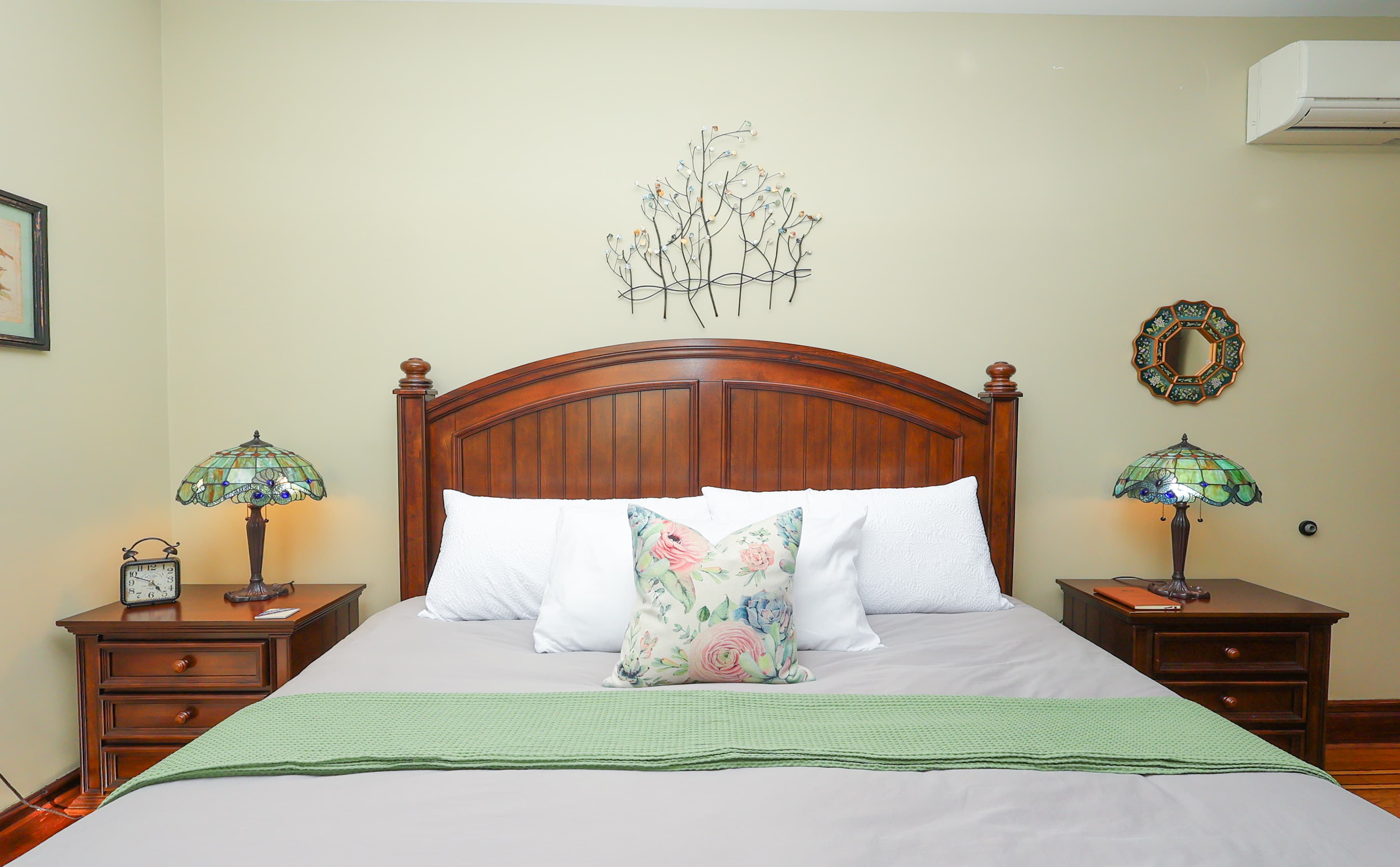 A cozy bedroom featuring a wooden headboard, decorative lamps, and a green accent throw.