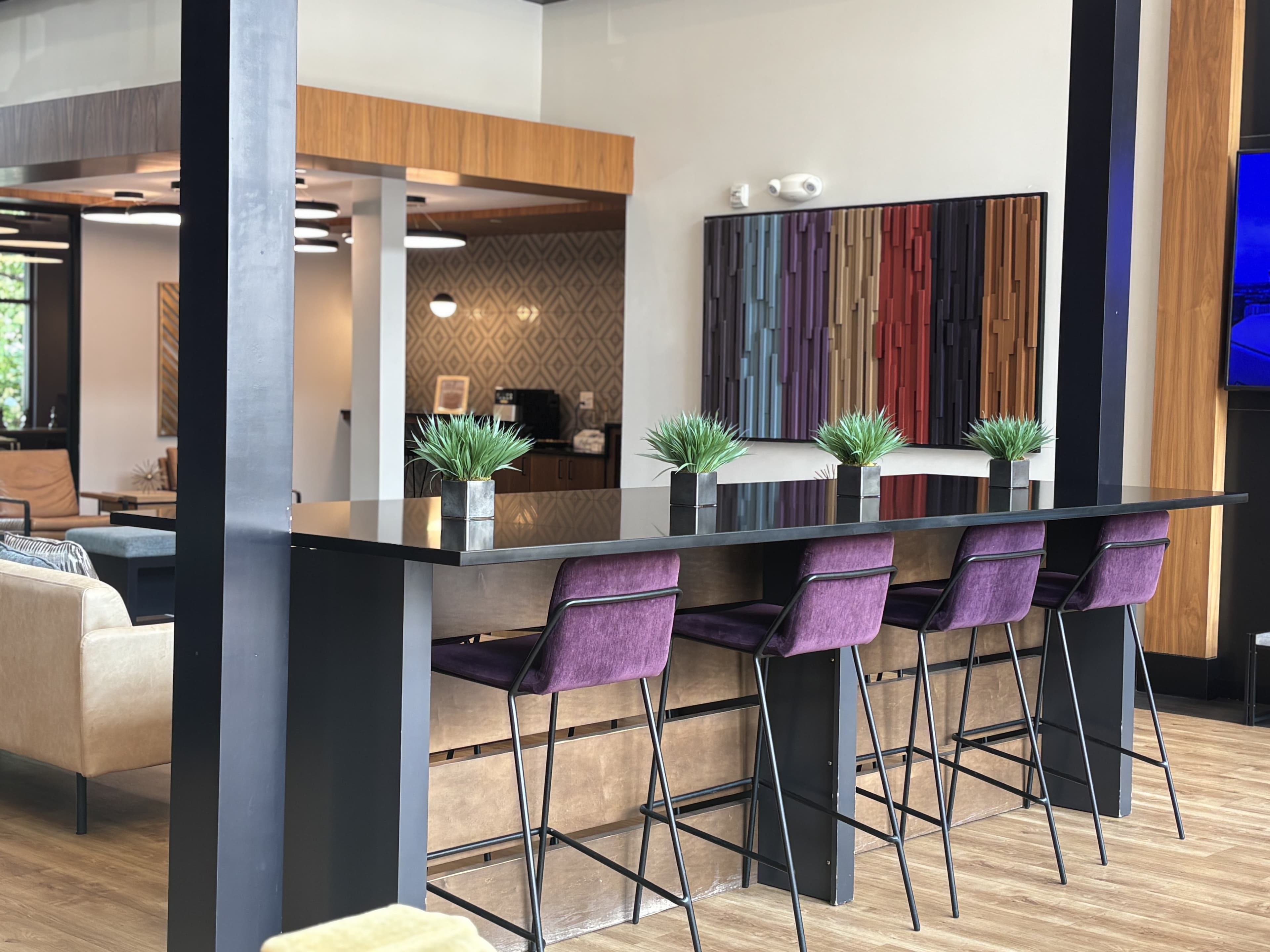 A modern bar area with purple stools and decorative plants, set in a stylish lounge.