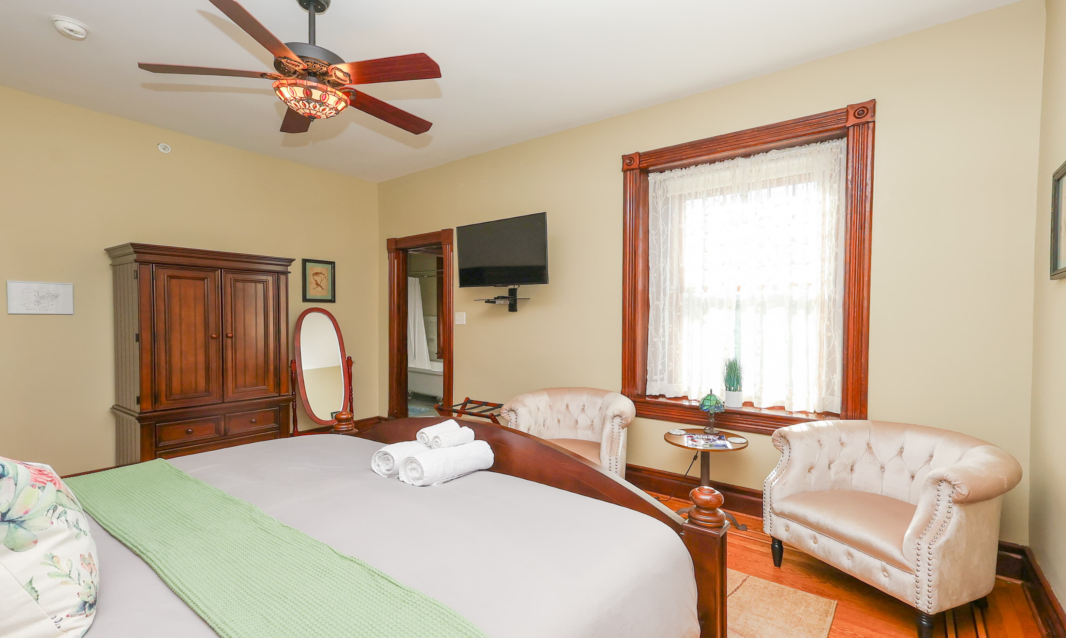 Cozy bedroom featuring a large bed, decorative green blanket, seating area, and natural light from a window.