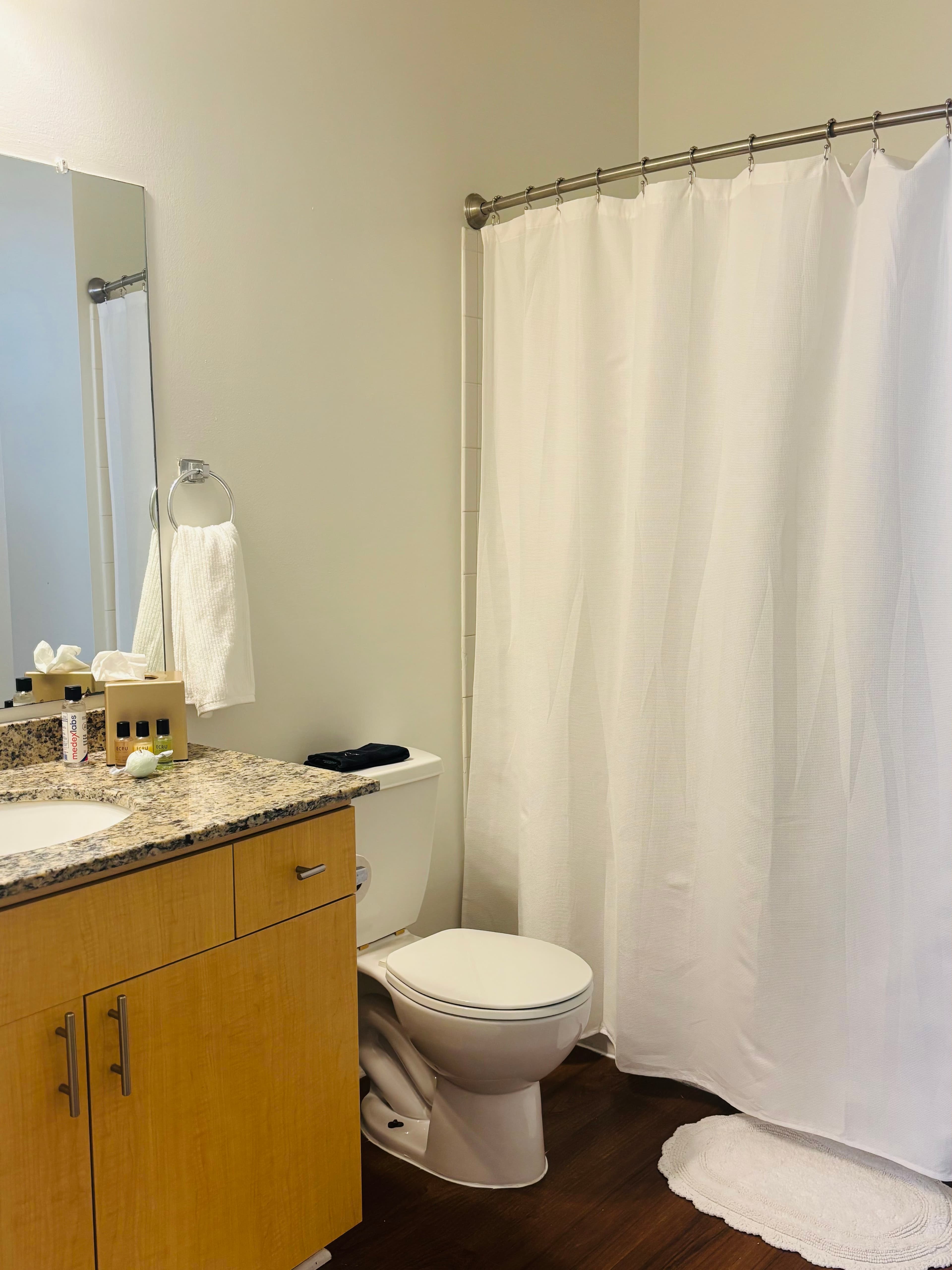 A modern bathroom featuring a toilet, a granite countertop with toiletries, a mirror, and a shower curtain.
