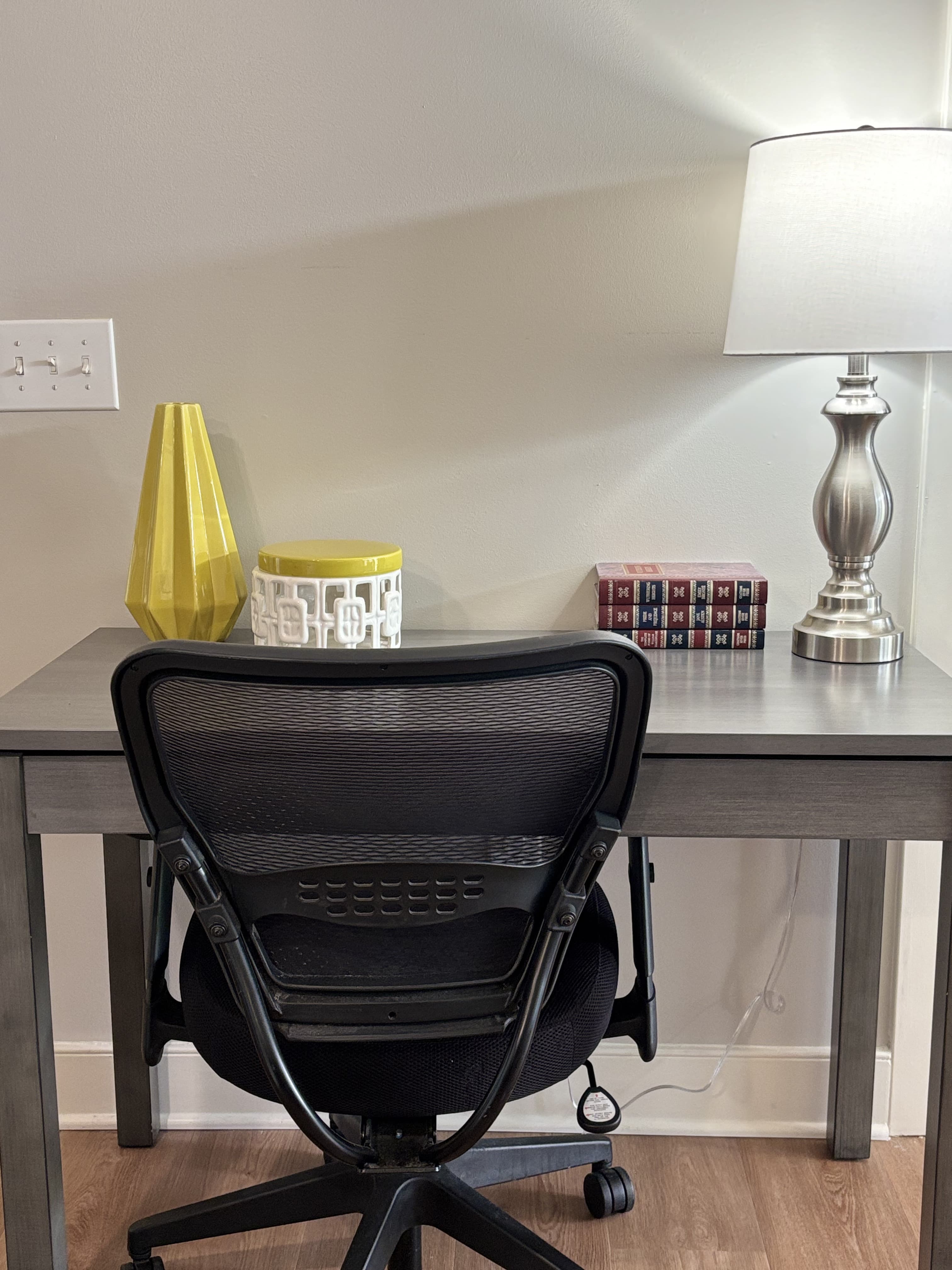 A modern desk setup featuring a black office chair, decorative vases, a lamp, and a stack of books.