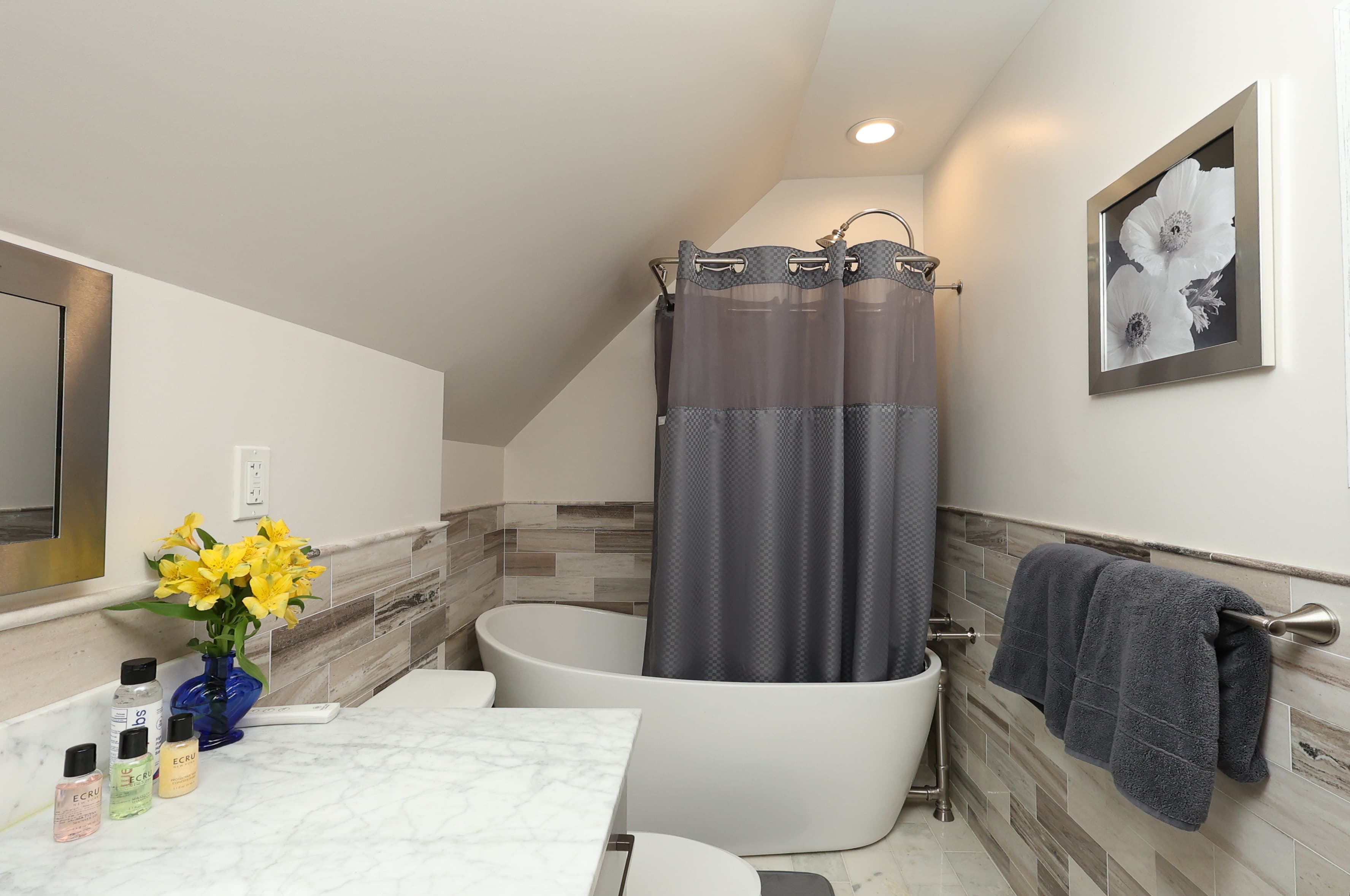 A modern bathroom featuring a freestanding tub, gray shower curtain, and a marble countertop with flowers.