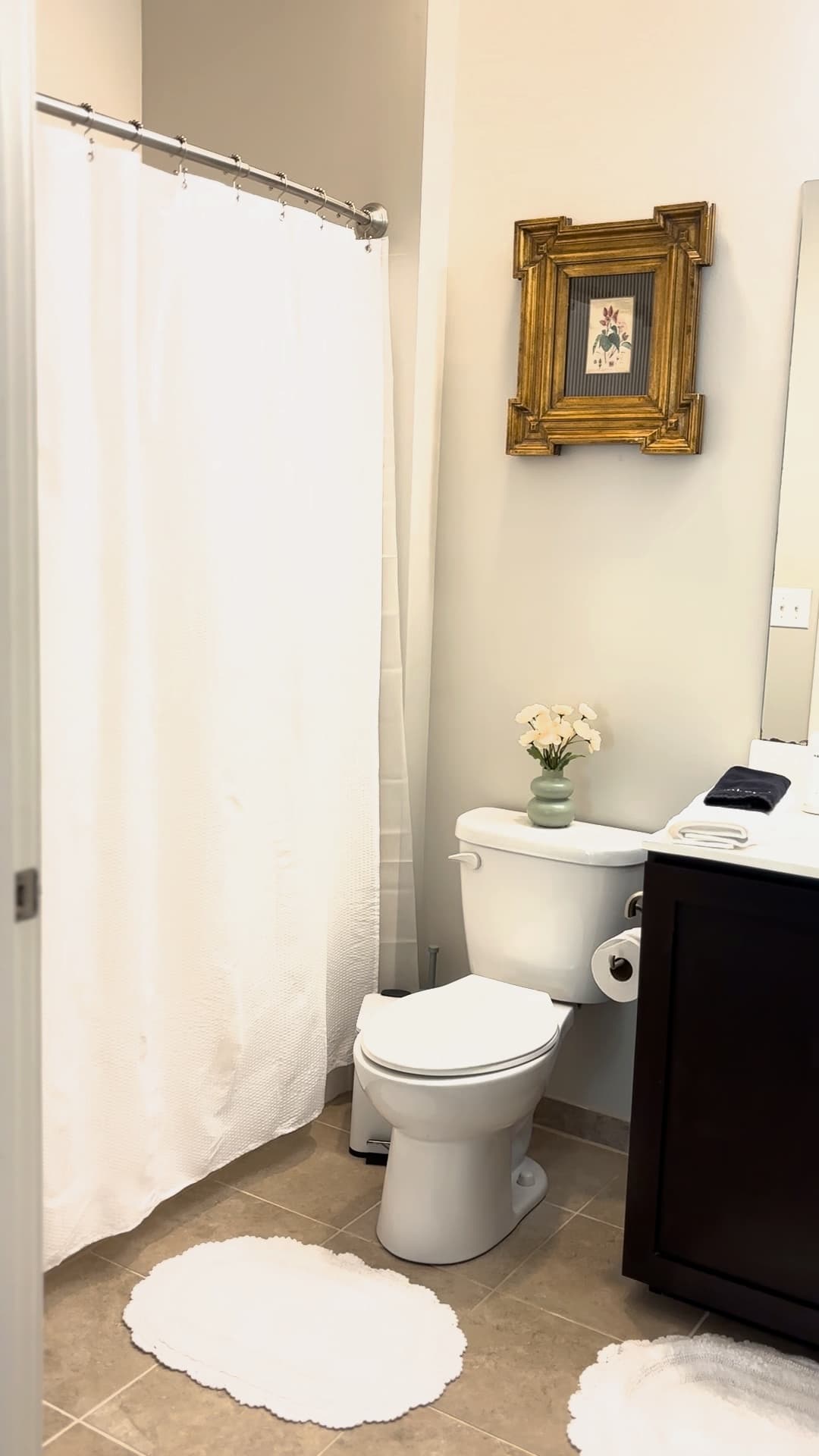 A clean bathroom with a toilet, white shower curtain, and a decorative framed flower print on the wall.