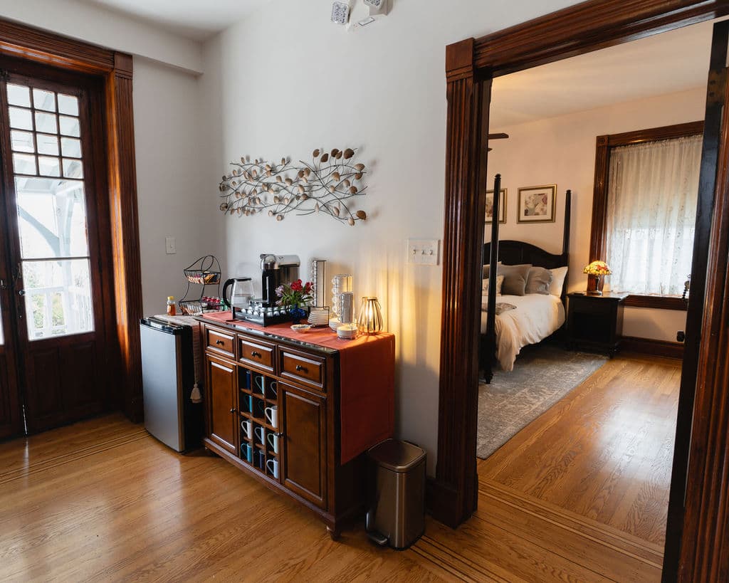 A cozy entryway featuring a wooden sideboard with a mini-fridge and decor, leading to a well-lit bedroom.