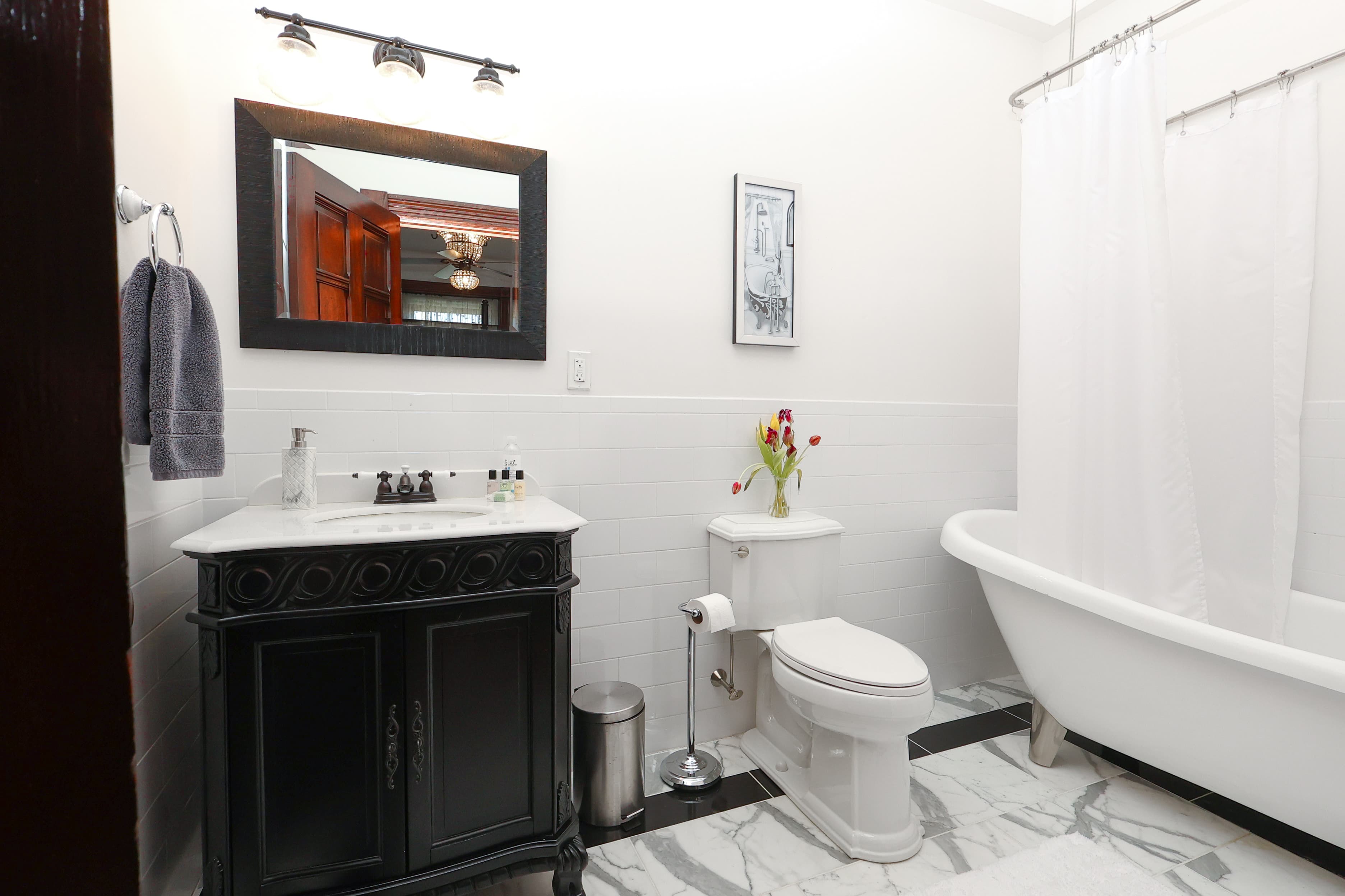 A modern bathroom featuring a black vanity, white bathtub, and marble floor with a vase of flowers.