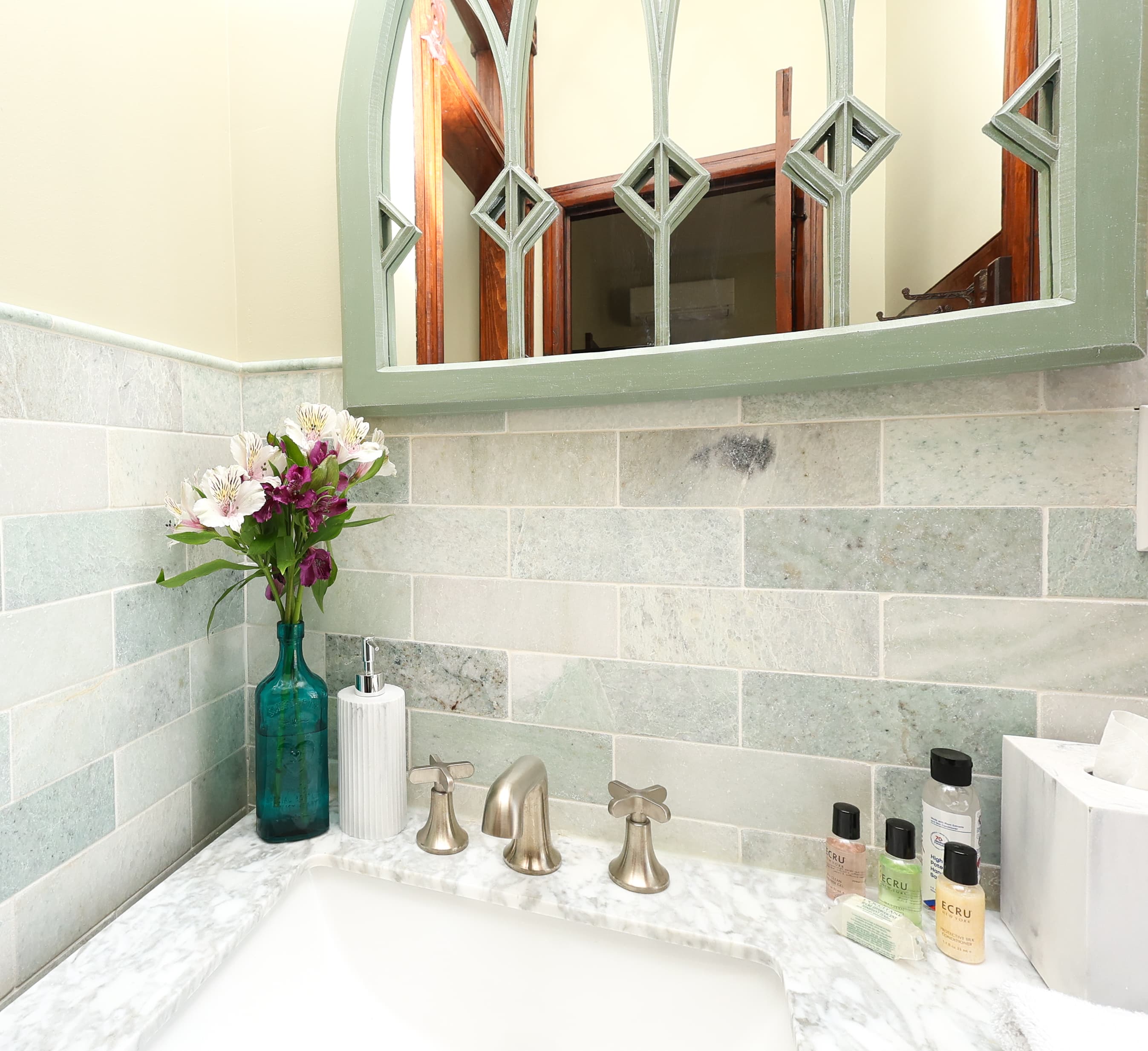 A bathroom sink area featuring a decorative mirror, floral arrangement, and various toiletries on a marble countertop.