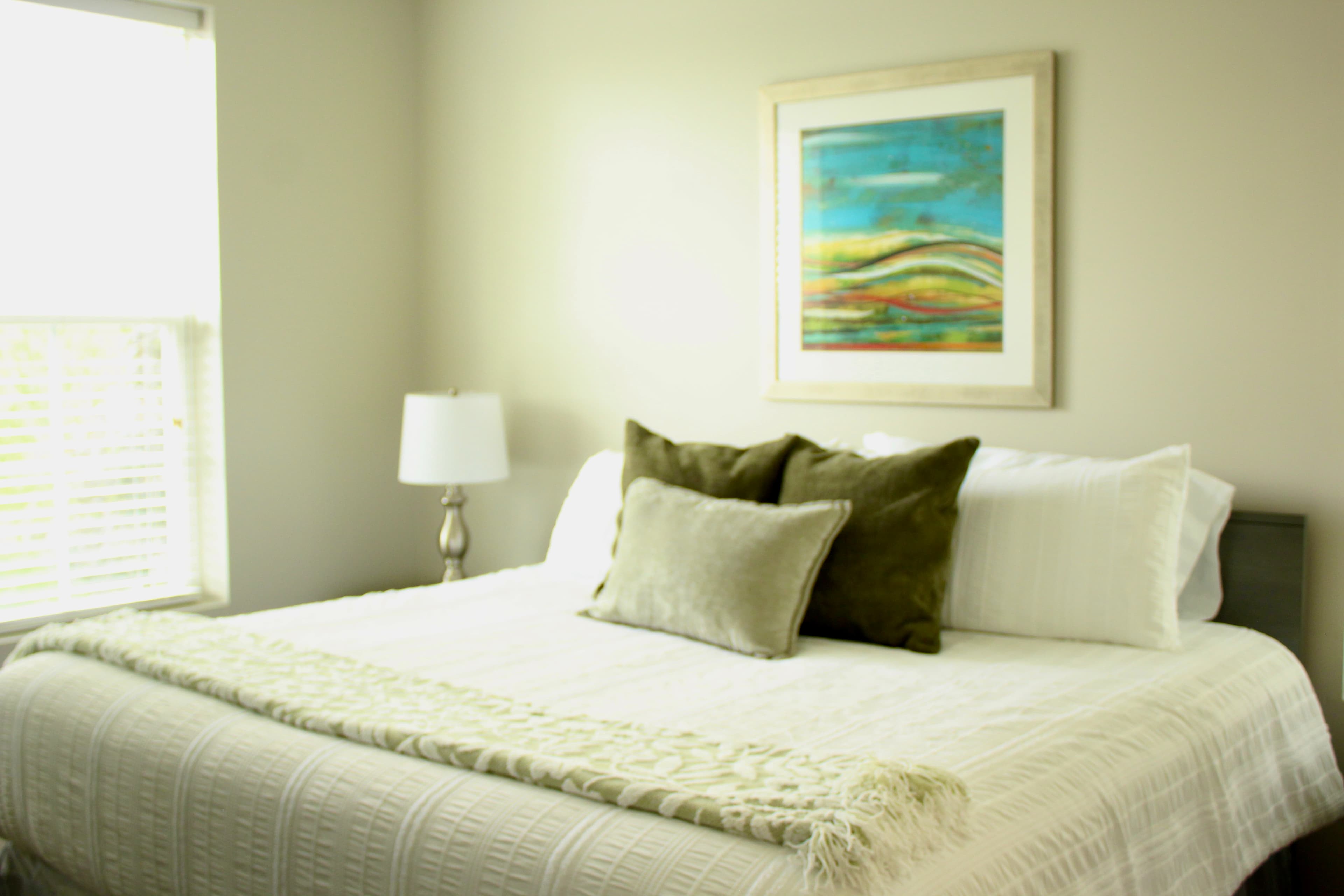 A cozy bedroom featuring a neatly made bed with decorative pillows and a colorful abstract painting on the wall.