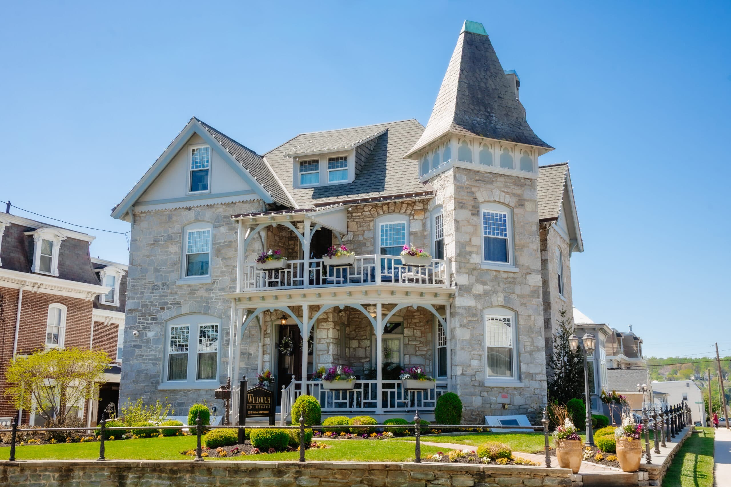 A large, ornate stone house with a turret and decorative balcony, surrounded by landscaped gardens under blue skies. A large, ornate stone house with a turret and decorative balcony, surrounded by landscaped gardens under blue skies.