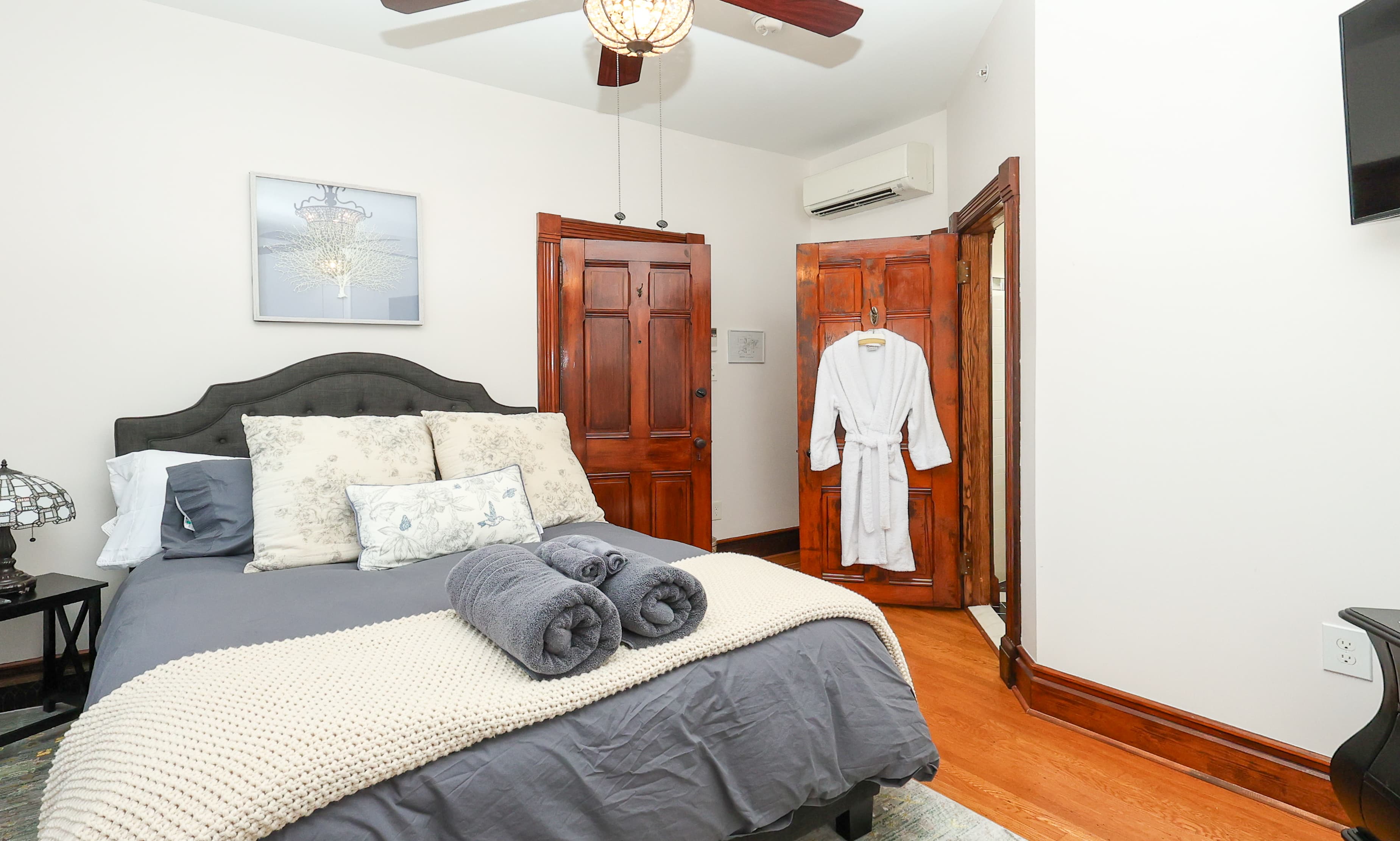 A cozy bedroom featuring a gray bedspread, decorative pillows, and a white robe hanging beside a wooden closet.