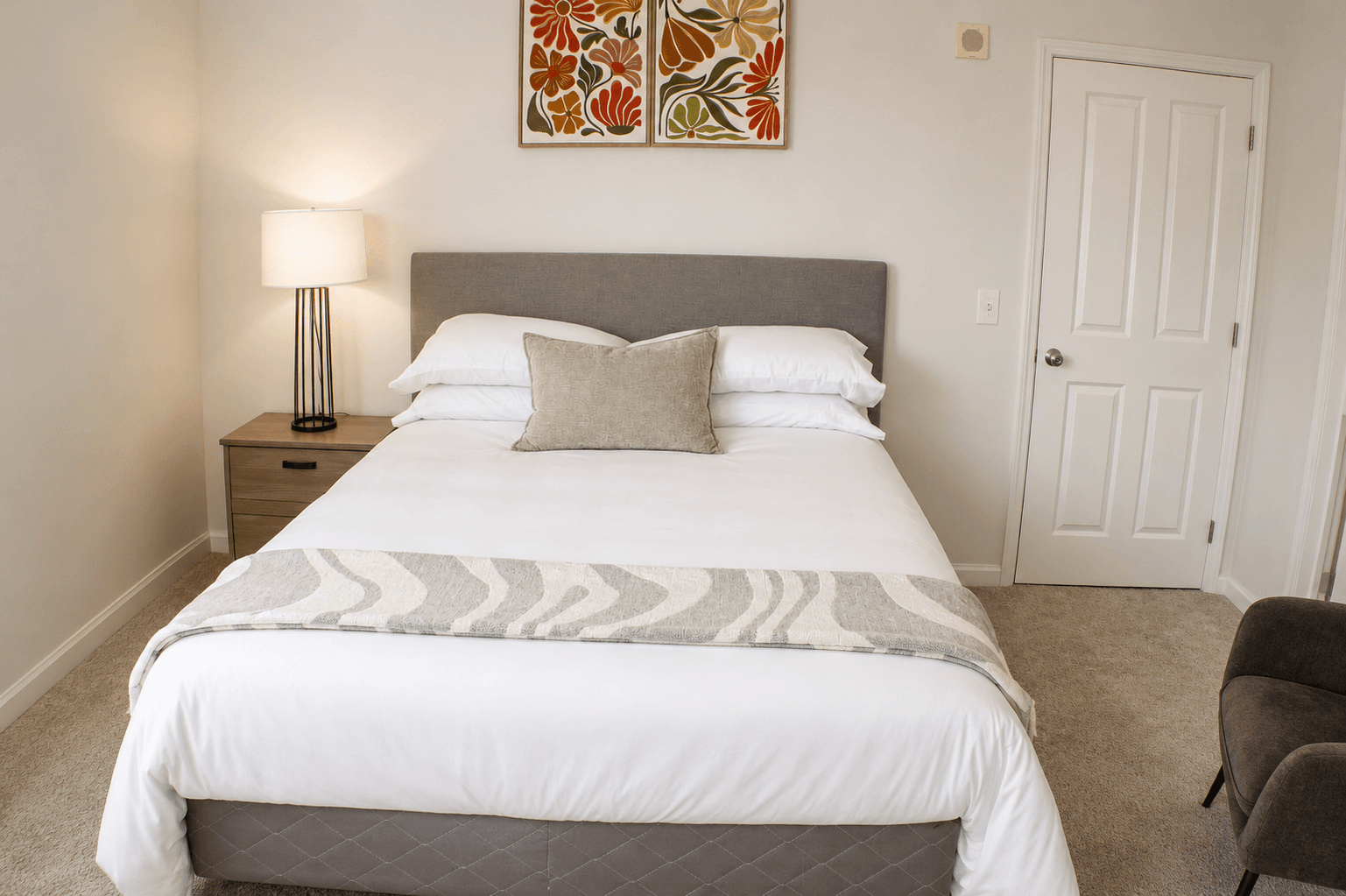 A cozy bedroom featuring a neatly made bed, a bedside lamp, and decorative wall art.